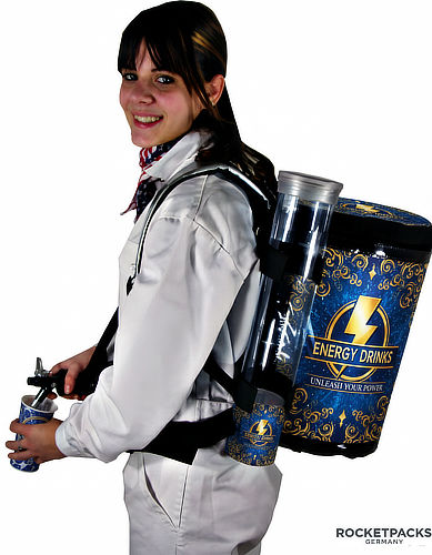 Promoter wearing a beverage dispensing backpack with blue energy drink advertising, holding a drink can beside the dispensing tap.